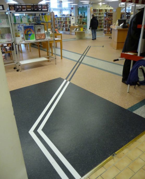 Tactile Flooring ledstråk aluminium 2 mm visar vägen fram till receptionen, med vit kontrastremsa på den mörka delen av golvet och med svart mot det ljusare golvet.