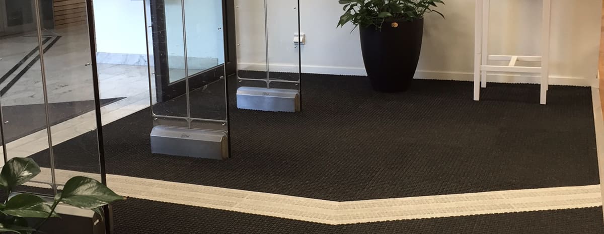 Visar entrémattan Combi Tile i svart med ett infällt vitt ledståk. Stråken har en tydlig taktil yta för att underlätta för personer med käpp.