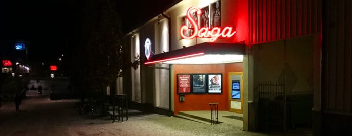 Entrén till Alingsås biograf Saga, med sin varmt välkomnande rödlysande neonskylt. Fotad en mörk höstkväll med ett tunt snötäcke på marken.