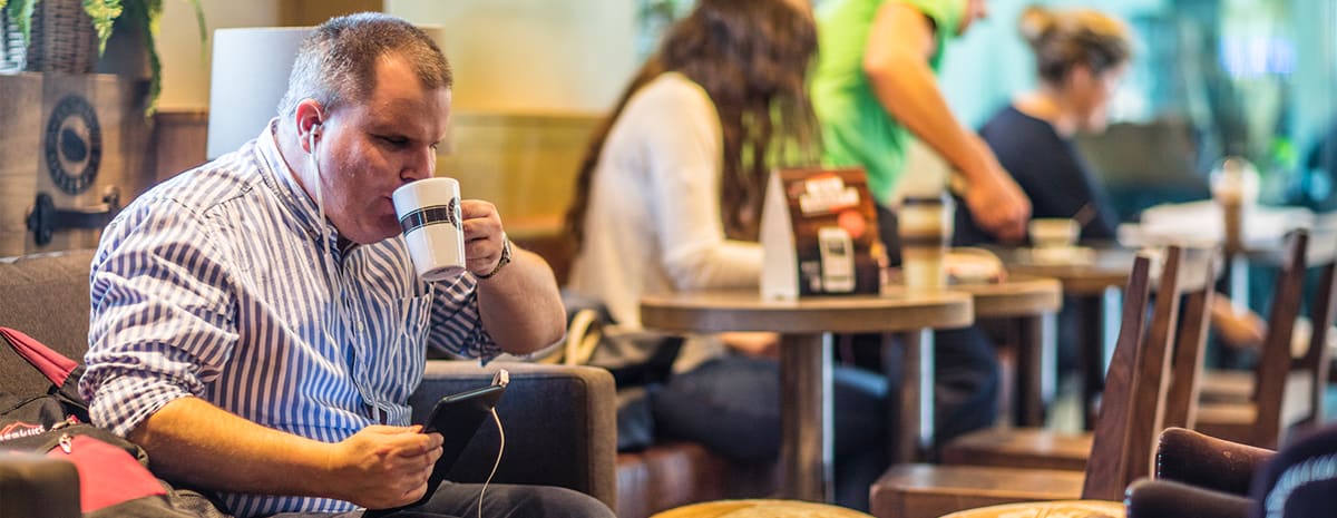 Fredrik sitter i soffan på cafét och dricker kaffe. I handen håller han sin smartphone.